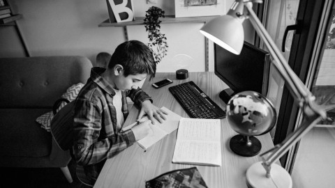 Student sitting at desk writing, computer and globe are nearby